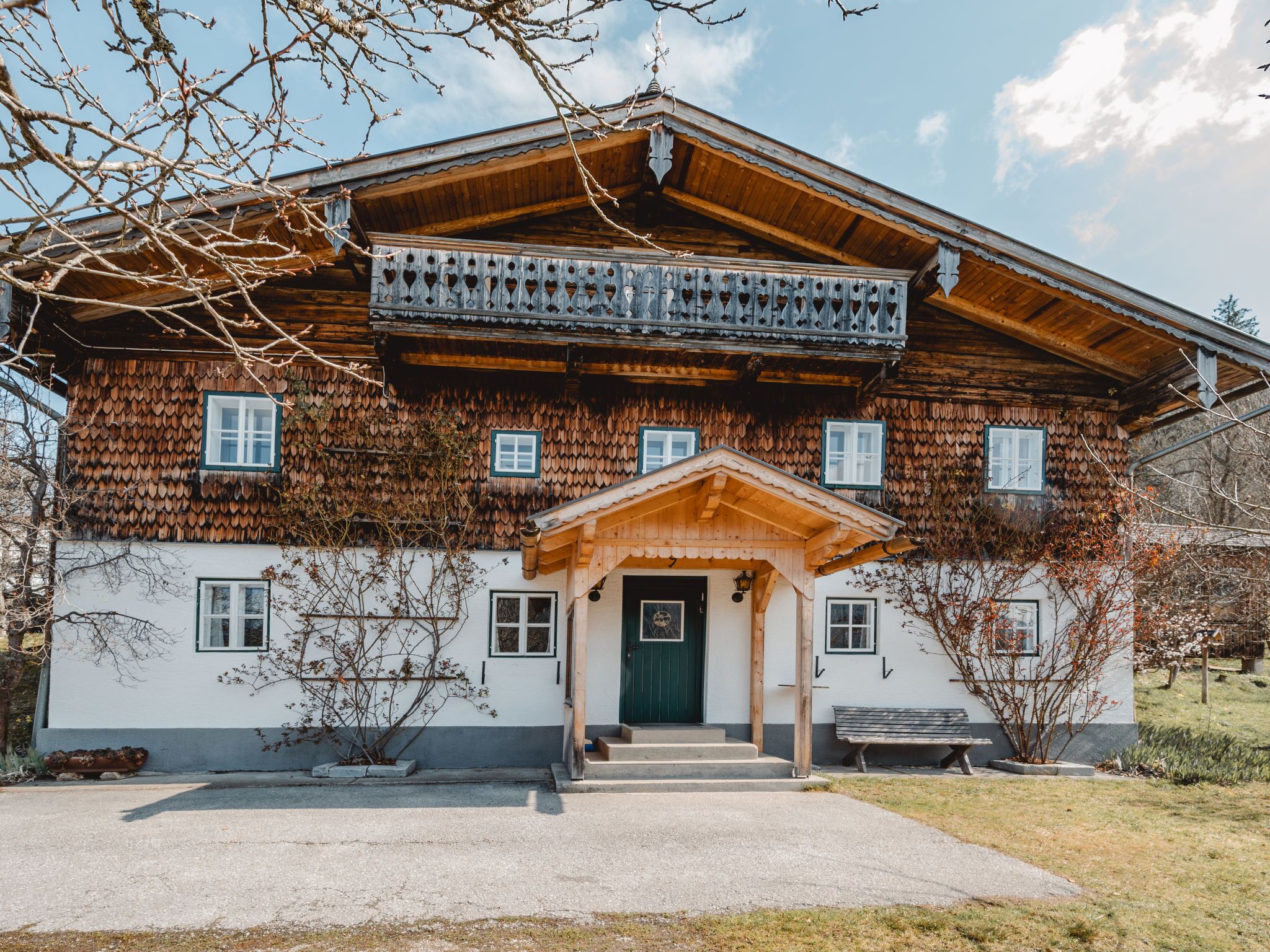 Une maison traditionnelle en bois, dotée d’un balcon, d’une porte verte et d’un banc à l’extérieur.