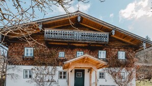 Una casa de madera tradicional con balcón, una puerta verde y un banco afuera.