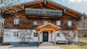 Ein traditionelles Holzhaus mit Balkon, grüner Tür und Sitzbank vor der Tür.
