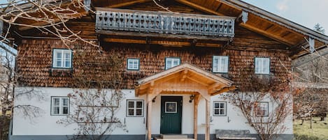 A traditional wooden house with a balcony, a green door, and a bench outside.
