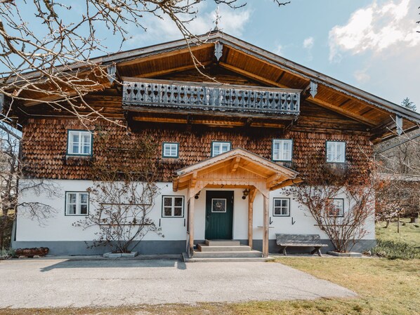 A traditional wooden house with a balcony, a green door, and a bench outside.
