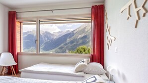 A bedroom with a bed, a view of mountains, and red curtains. - Apartment Zenkei by Interhome (Leontica)