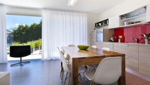 A modern kitchen with a wooden dining table, white chairs, and a red accent wall. - Apartment Zenkei by Interhome (Leontica)