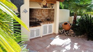 An outdoor kitchen area with a brick backsplash, wooden pergola, and a decorative sun emblem. - Vacation home Calina by Interhome (Benissa)