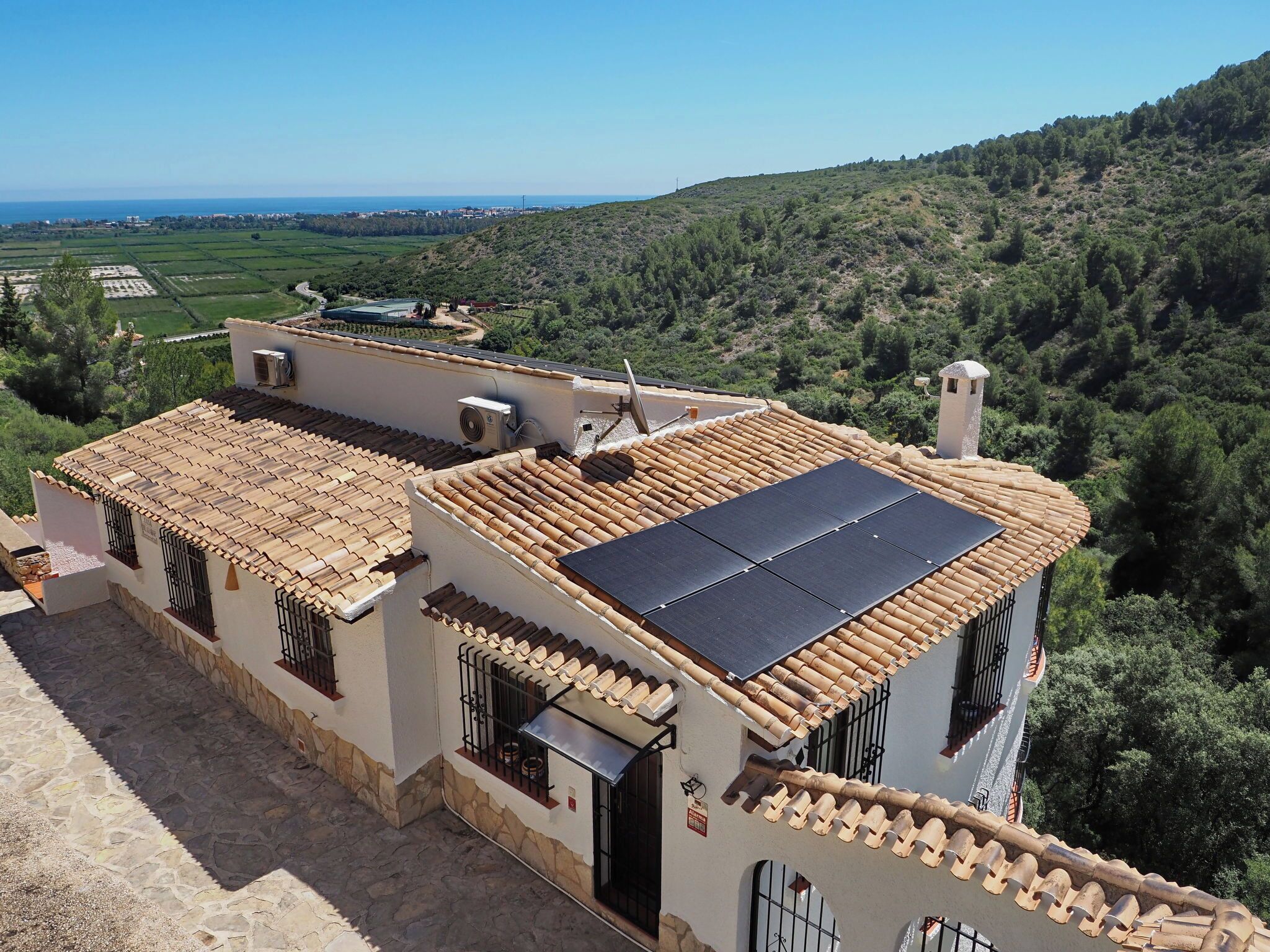 A building with a tiled roof, solar panels, and a view of a hilly landscape.