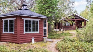 Une cabane à l’extérieur rouge et aux bordures blanches, entourée d’une forêt dense.
