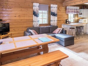 A cozy cabin interior with a wooden interior, a sofa, a dining table with placemats, a television, and a kitchen area. - Rukatörmä, kesäjärvi by Interhome (Kuusamo)