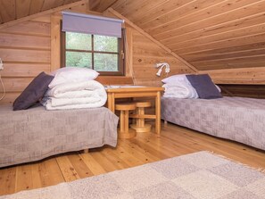 Un ambient acollidor a una habitació de cabana amb dos llits, una taula de fusta petita i una finestra amb vista als arbres.