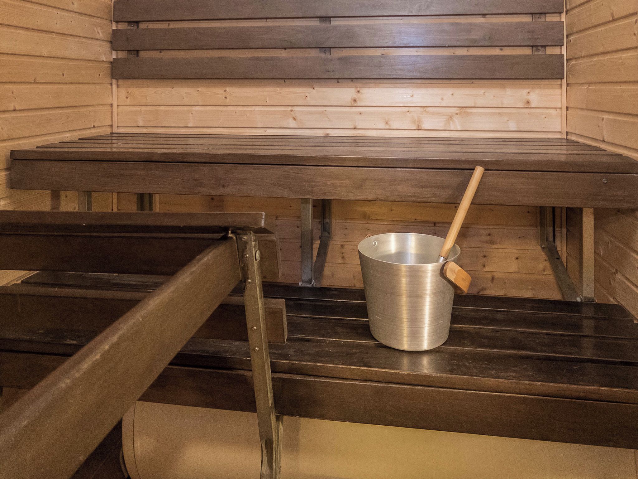 Una sauna con bancos de madera y un cubo de metal con asa de madera.