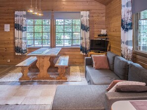 Interior acolhedor de uma cabana com mesa de madeira e bancos, um sofá e uma televisão.