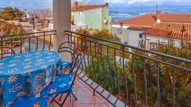 A balcony with a table and chairs, overlooking a residential area with houses and a distant view of the sea. - Vacation home Ivan by Interhome (Krk/Šilo)