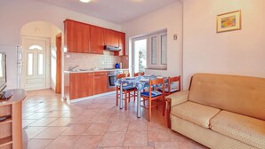 A spacious living area with a sofa, a dining table with chairs, a kitchen with wooden cabinets, and a TV. - Vacation home Ivan by Interhome (Krk/Šilo)