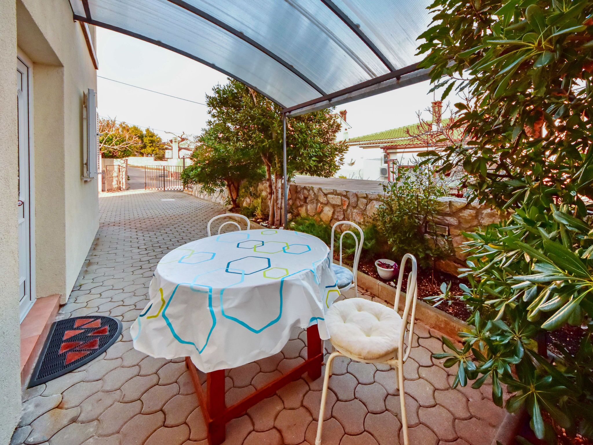 Eine überdachte Terrasse mit rundem Tisch und Stühlen, einer Steinmauer und einem Baum.