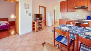 A compact kitchen with wooden cabinets, a dining table set for two, and a television in the corner. - Vacation home Ivan by Interhome (Krk/Šilo)