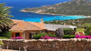 A stone-walled building with a tiled roof overlooking a coastal area with boats and a clear blue sea. - Paradiso by Interhome (Porto Cervo)