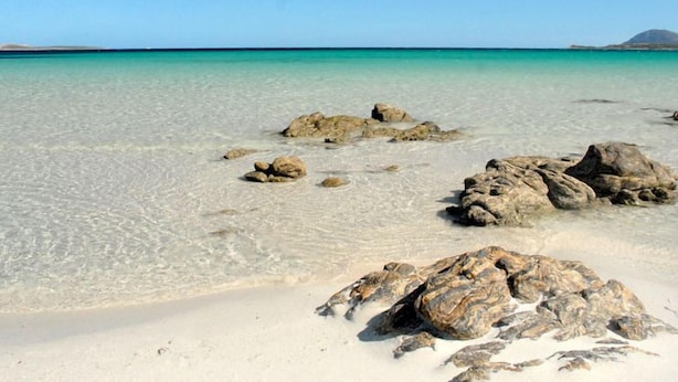 A beach with clear turquoise water, scattered rocks, and a distant mountain. - Paradiso by Interhome (Porto Cervo)
