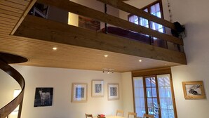 Une pièce avec un plafond en bois, une table à manger entourée de chaises et des tableaux encadrés accrochés aux murs.