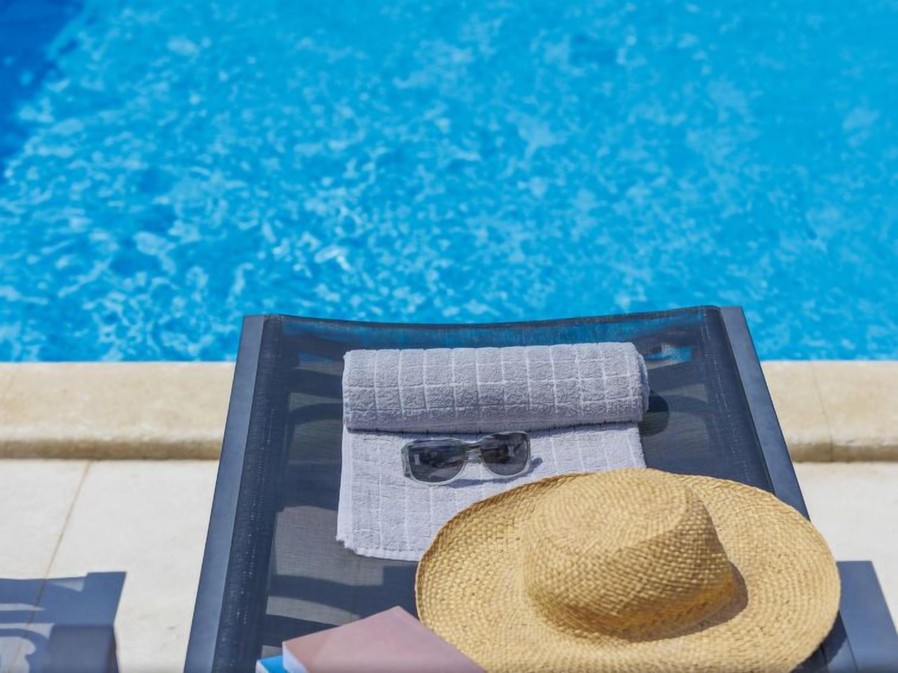 Une chaise longue placée au bord de la piscine, avec une serviette pliée, des lunettes de soleil et un chapeau de paille.