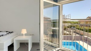 Een balkon met een glazen deur, een kleine tafel met een lamp en uitzicht op een zwembad.