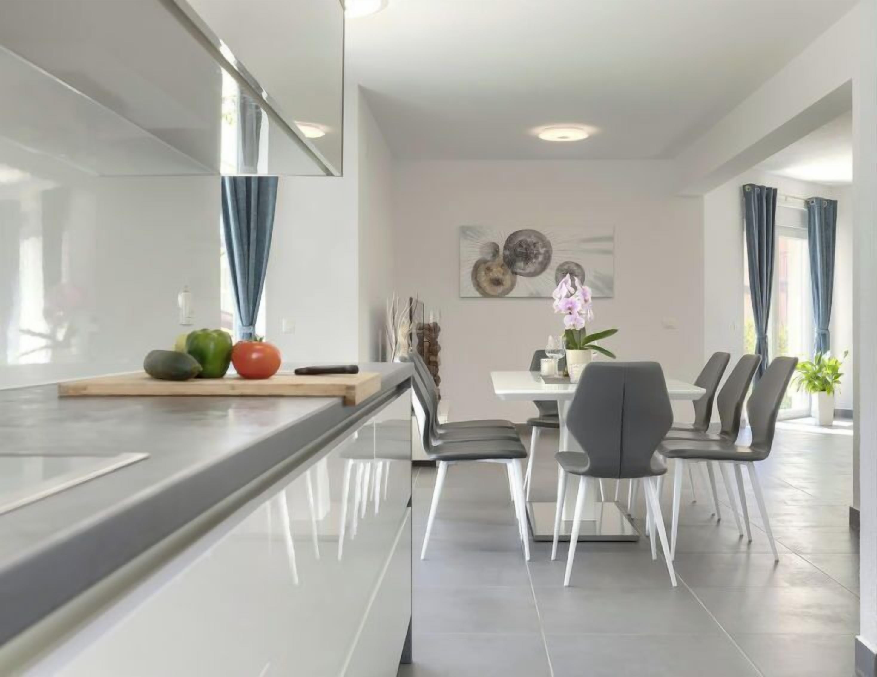 A modern kitchen with a central island, dining area with chairs, and a table.