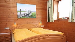 A wooden bed with a headboard, two bedside tables, a window with curtains, and a painting of a beach on the wall. - Annelies by Interhome (Aschau im Zillertal)