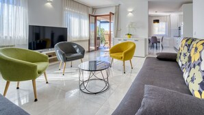 A modern living room with a sofa, two armchairs, a coffee table, and a TV.