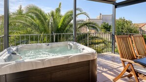 A hot tub on a balcony with a view of palm trees and a building in the background.