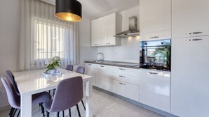 A modern kitchen with white cabinets, a black hanging light, and a view of the outdoors through the window.