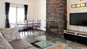 Una sala de estar con chimenea de piedra, un televisor de pantalla plana, una mesa de centro de vidrio y una zona de comedor con mesa y sillas.