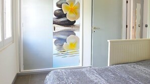 Una habitación con una cama, una puerta con un panel de vidrio que presenta un diseño de piedra y flores, y vista a otra habitación con una cama.
