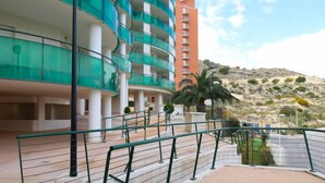 Un hotel de varios pisos con diseño moderno, que cuenta con balcones con barandillas de vidrio y vistas a un paisaje montañoso.
