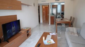 Una sala de estar moderna con una televisión de pantalla plana, una mesa de centro de madera, un sofá y un comedor con una mesa y sillas.
