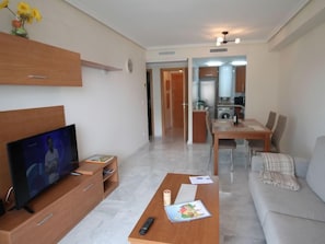 A modern living room with a flat-screen TV, a wooden coffee table, a sofa, and a dining area with a table and chairs.