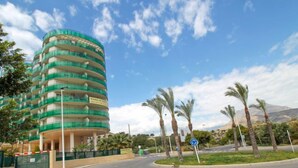 Un hotel de varios pisos con fachada curva, situado en una intersección con palmeras y cielo despejado.