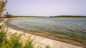 Une plage côtière aux eaux limpides, bordée d’un rivage sablonneux et parsemée de quelques zones verdoyantes.