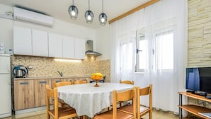 Une cuisine compacte avec des meubles blancs, un pare-feu en carreaux et un coin repas comprenant une table ronde et des chaises en bois.