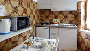 Cocina compacta con microondas, hervidor y cafetera sobre la encimera, un lavamanos y un pequeño comedor con una mesa preparada para dos personas.