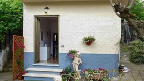 Una casa con fachada blanca y azul, una puerta de madera, un pequeño porche con escalones, una estatua y una maceta colgante.