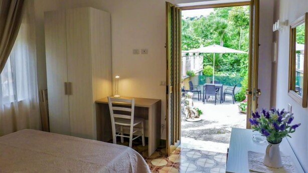 Un dormitorio con cama, escritorio y puerta abierta que da a un patio exterior con mesa y sillas.