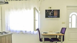 A dining area with a table set for two, a window with curtains, and a television mounted on the wall. - Vacation home Ana by Interhome (Novigrad (Zadar))