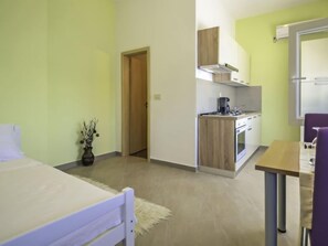 A compact hotel room with a bed, a small kitchenette, a dining area, and a bathroom.