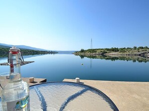 A clear view of a calm lake with a distant power line tower, a bottle of water, and a glass table.