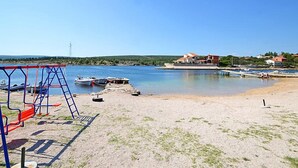 A beach with a swing set, boats, and a house with a red roof. - Vacation home Ana by Interhome (Novigrad (Zadar))