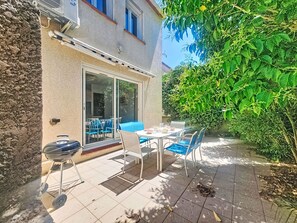 A patio with a table and chairs, a barbecue grill, and a sliding glass door leading to an indoor area.