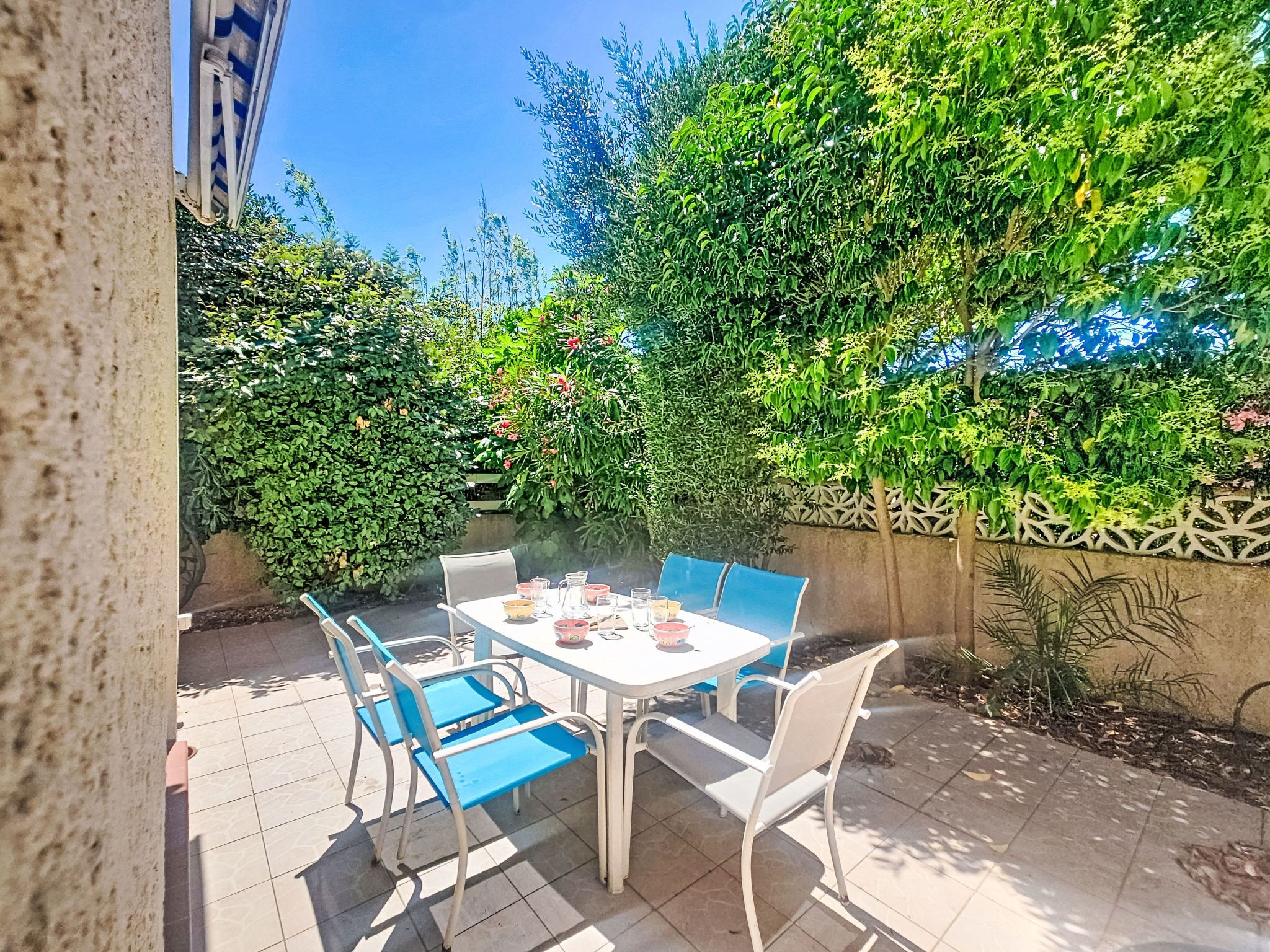 Une terrasse extérieure avec une table et des chaises, entourée d’une végétation luxuriante et agrémentée d’un mur décoratif.