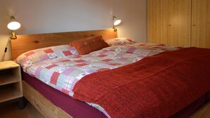 A bedroom with a wooden headboard, a bed with a patterned quilt, two bedside lamps, and a wooden wardrobe. - Apartment Oehrli by Interhome (Gstaad)