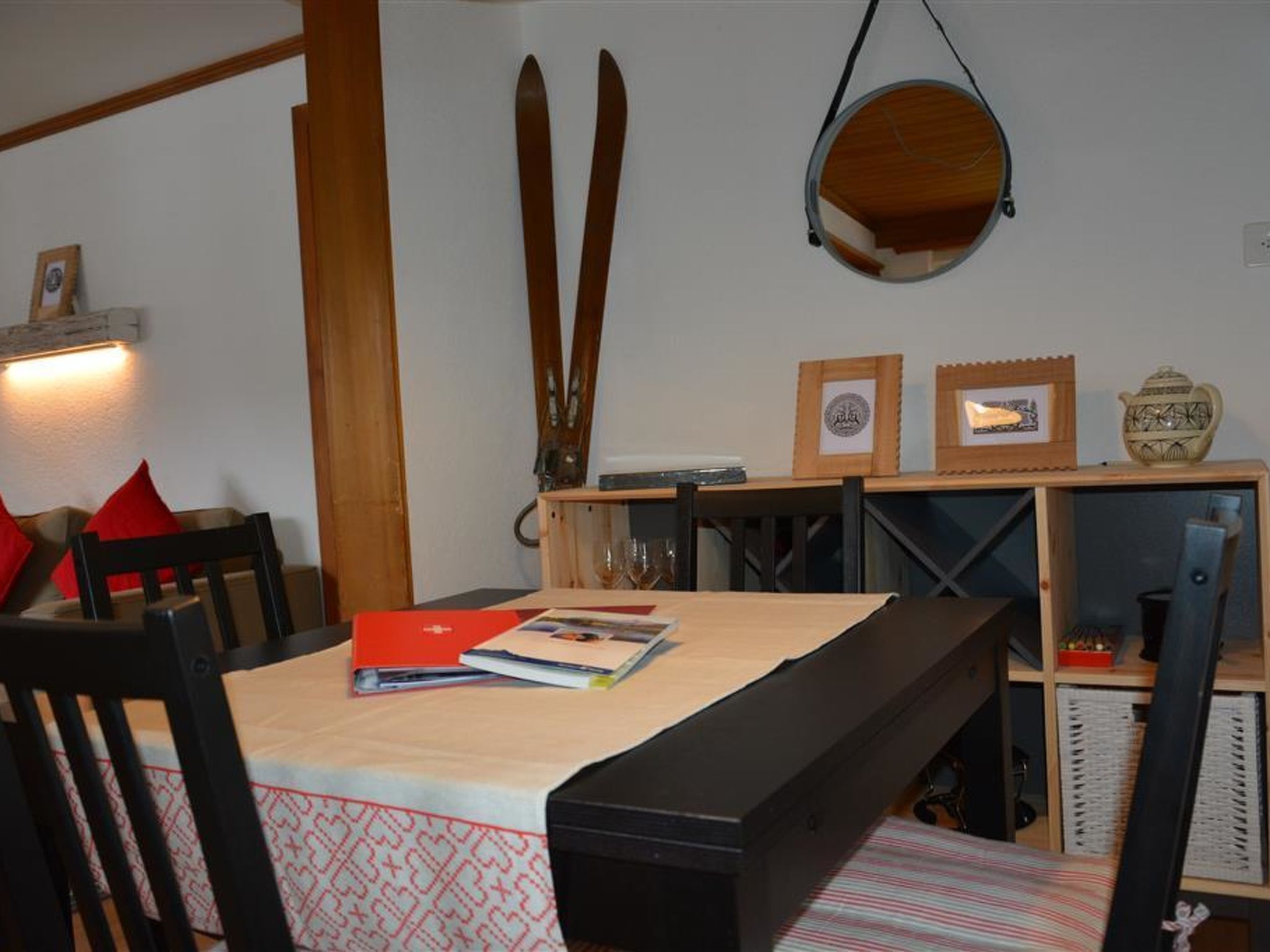 Ein Essbereich mit Tisch für zwei Personen, Holzstühlen, einer Bank und einem hängenden Spiegel.