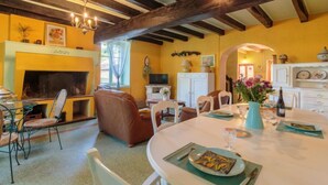 A cozy living room with a fireplace, wooden beams, and a dining area with a table set for two. - Le Jardin de Timothee by Interhome (Montmorillon)