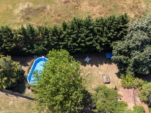 Vue aérienne d’un quartier résidentiel avec une piscine, une terrasse dotée d’une table et de chaises, et une végétation luxuriante qui entoure la propriété.
