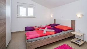 A bedroom with a wooden bed, a small bedside table, a nightstand, a window, and a light fixture. - Apartment B&B by Interhome (Medulin/Ližnjan)